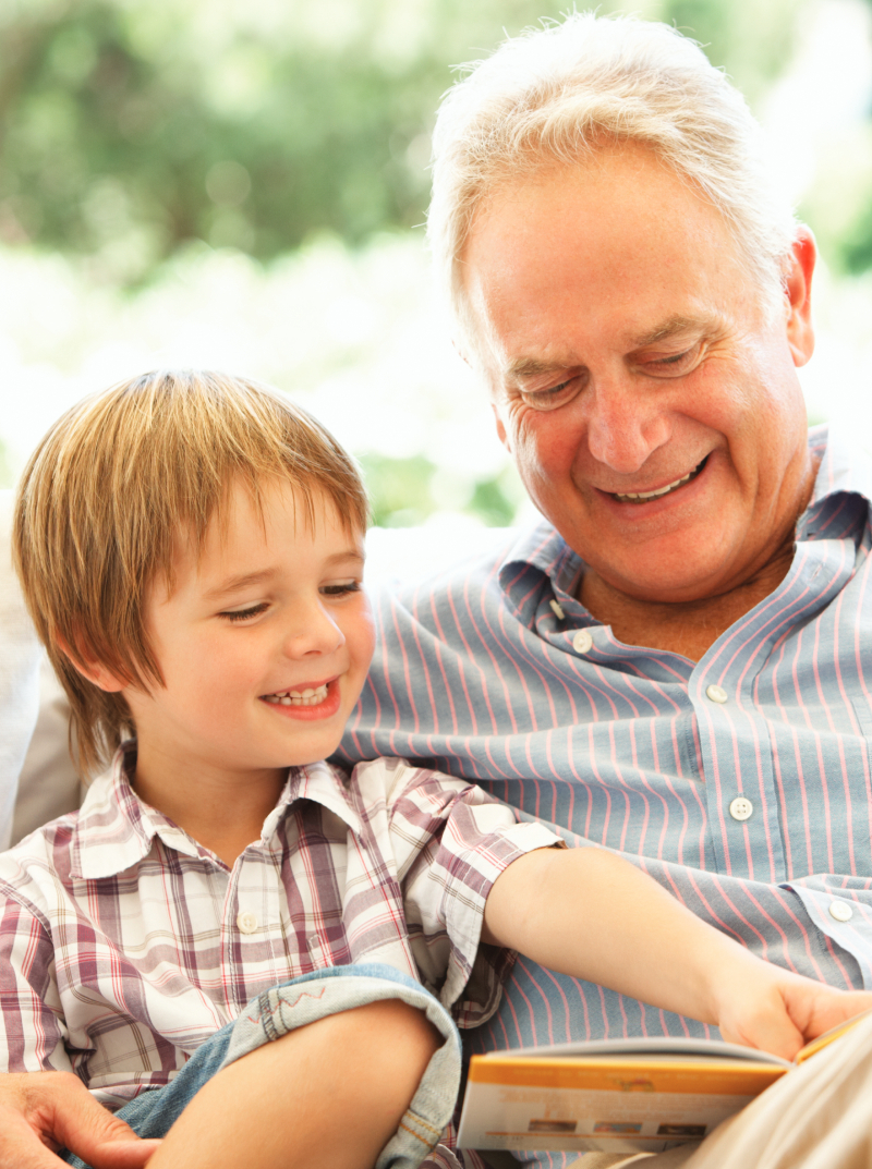 Starý otec s vnukom sedí vonku na lavici a čítajú rozprávky