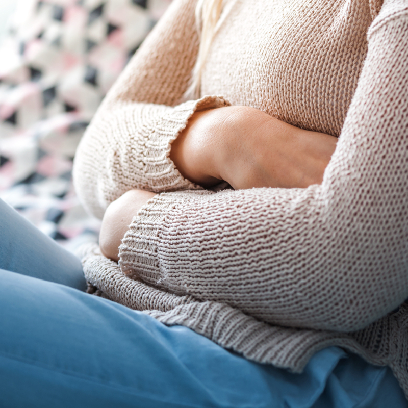 Sediaca žena na gauči a držiaca sa za brucho