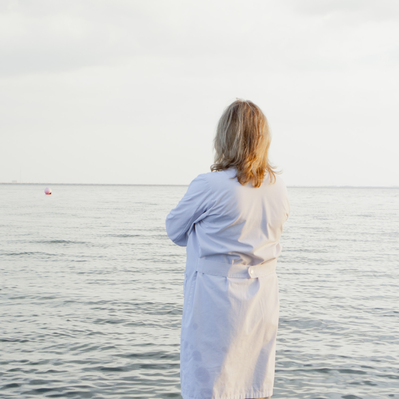 Žena v bielom župane, stojaca vo vode na pláži