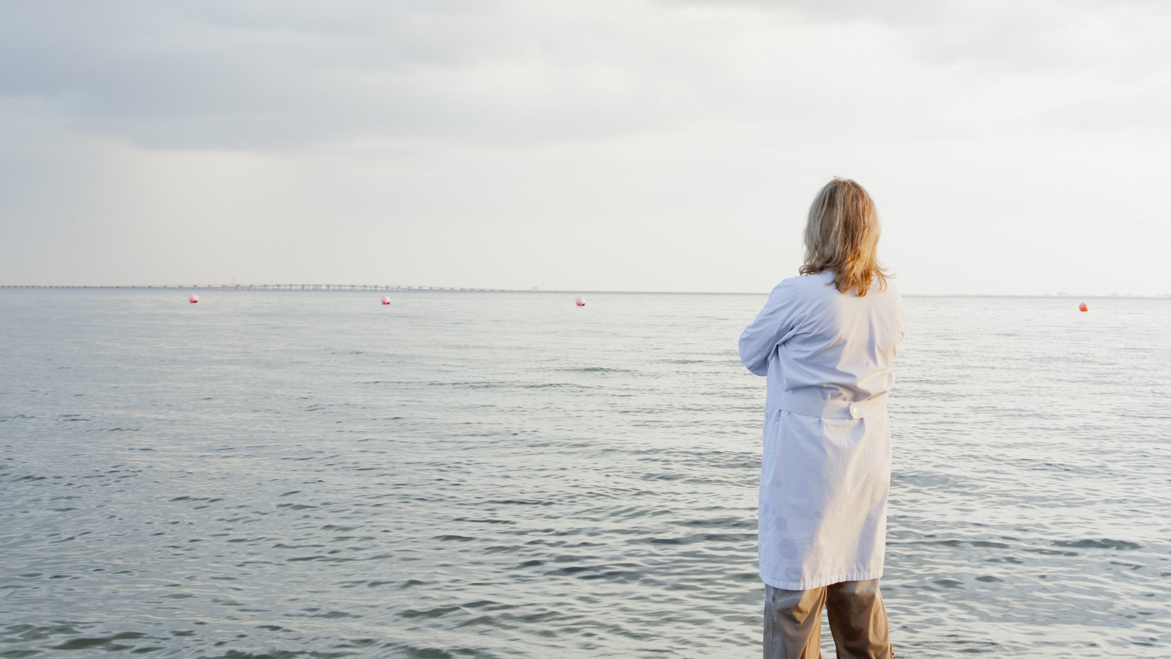 Žena v bielom župane, stojaca vo vode na pláži